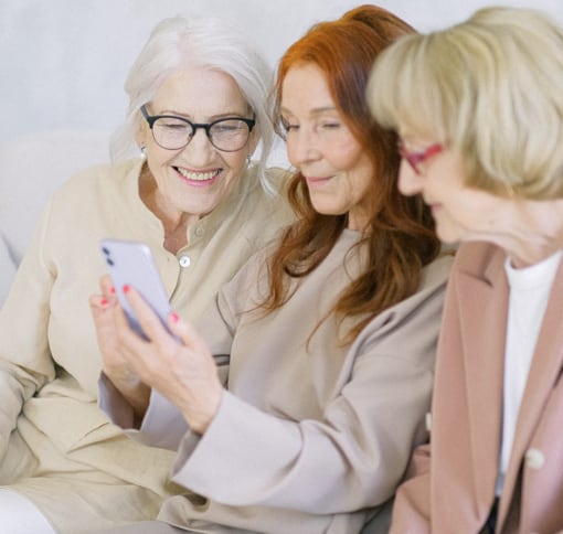 A trio of women happily conversing with an unknown person through a smartphone.